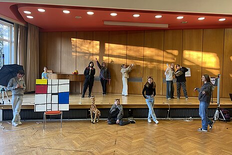 Schülerinnen und Schüler stehen auf einer Bühne in einer Schulaula